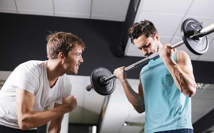 Young man motivating gym buddy during bicep exercise